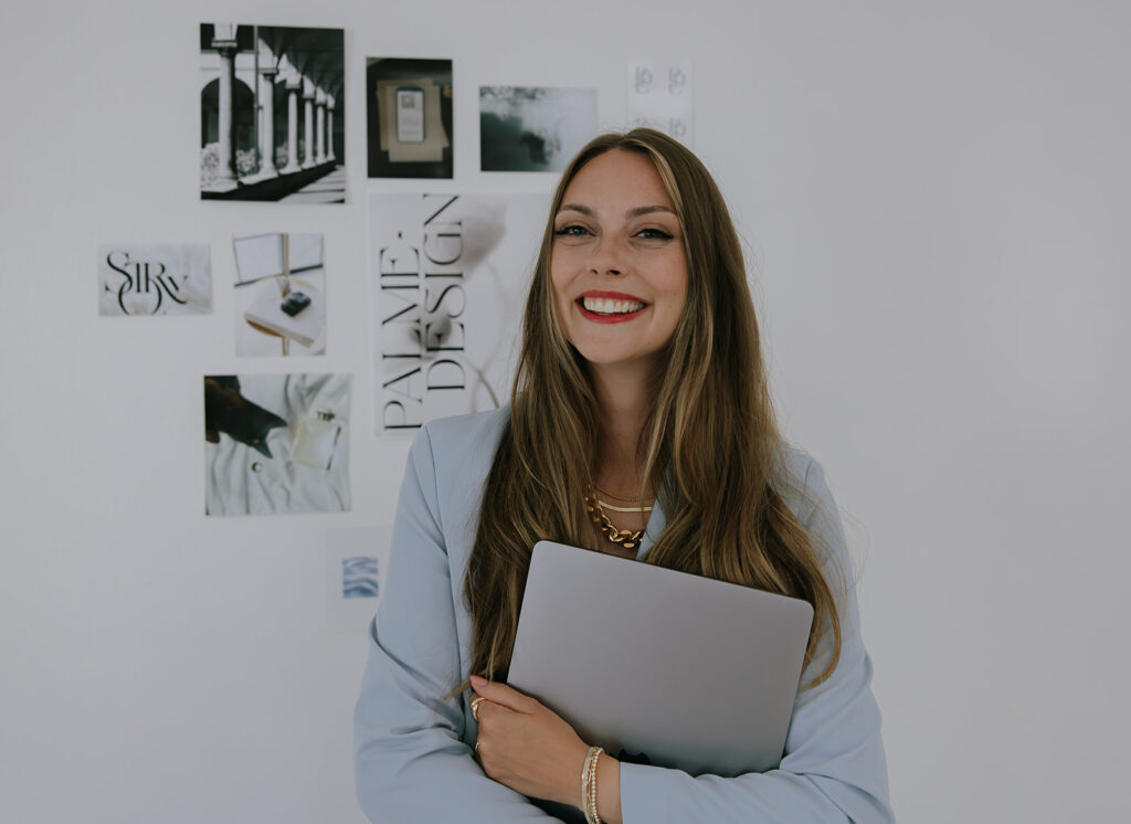 Kara holding laptop standing in front of mood board for photographers smiling