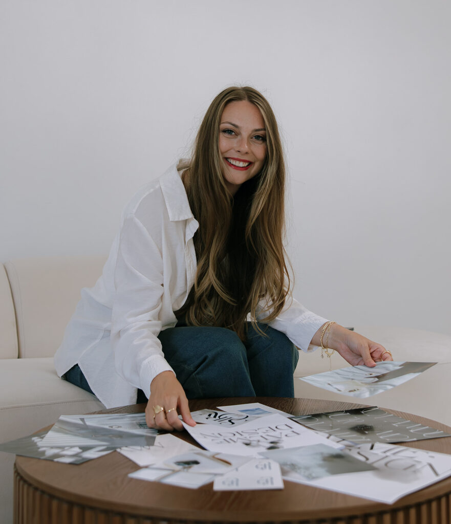 Kara Weech, owner of Palme Design Co, and Photographer Branding expert smiling sitting on a couch arranging images for a mood board.