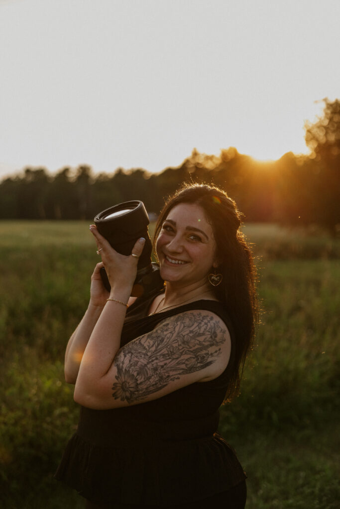 Image of Amanda in a field at golden hour holding her camera smiling.